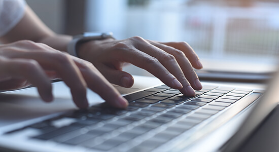 Zoomed-in picture of a woman's hands pressing keys on a laptop keyboard while browsing the web at a desk.