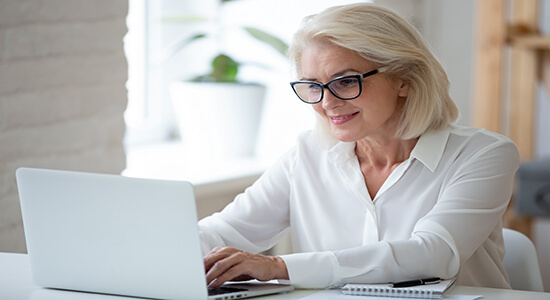 Concentrated businesswoman in glasses works at her desk typing on a laptop.